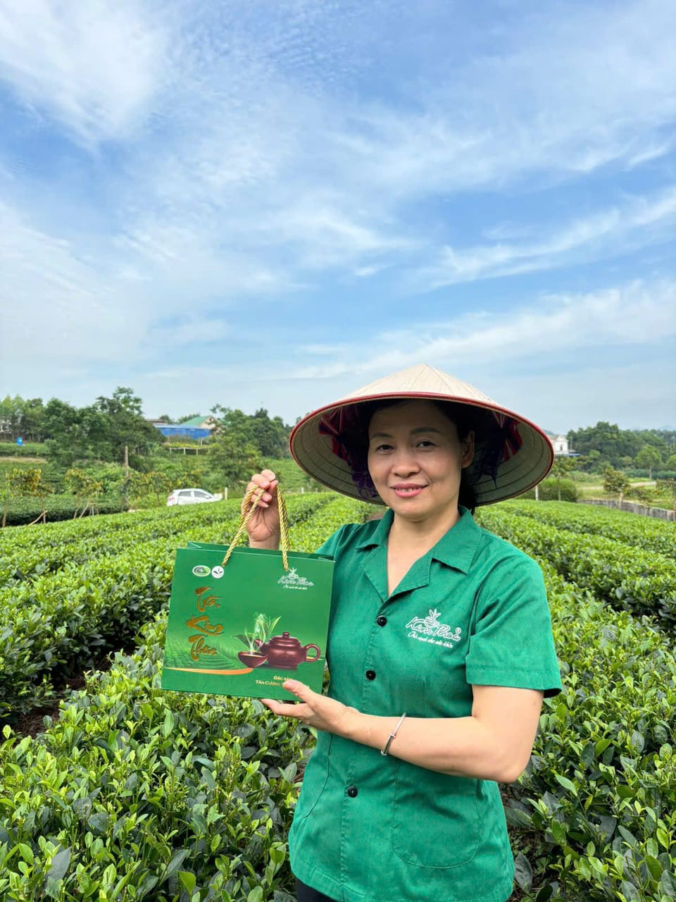 Cô Kim Thoa cầm túi quà Đinh Đinh đứng giữa đồi chè Tân Cương
